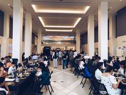 Large group of people at tables eating in high ceiling room.